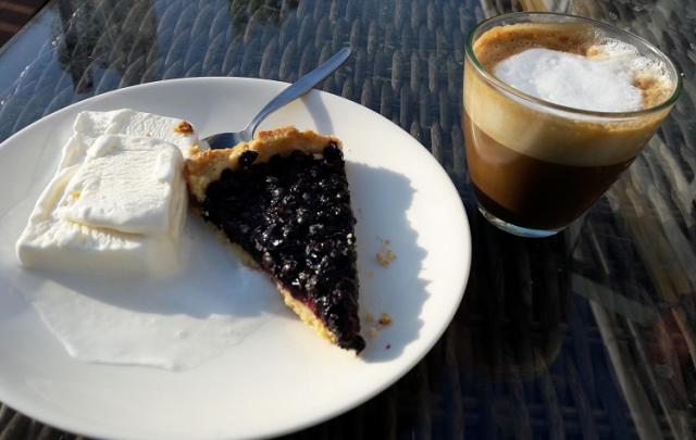 Ett glas med en cappuccino och ett fat med blåbärspaj och glass.