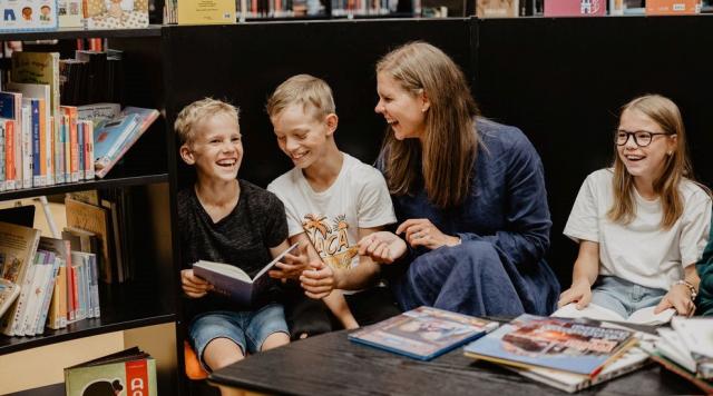 En glad Amanda Audas-Kass sitter och läser tillsammans med tre glada barn och en massa böcker.