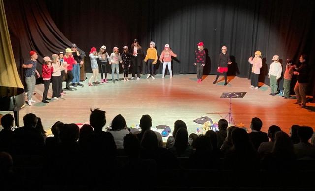 Ordkonsteleverna står på scenen och rappar. Publiken syns som silhuetter i förgrunden.