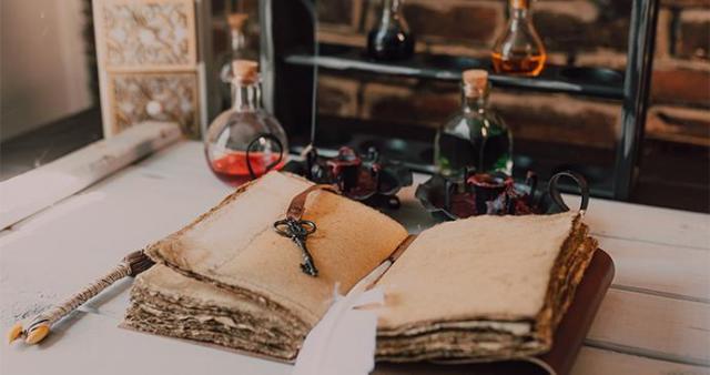 Ett gammaldags skrivbord med en mycket gammal, uppsalgen bok, en nyckel, en fjäderpenna och små flaskor med olika mixturer.