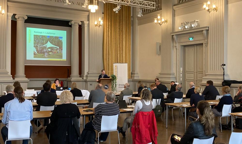 Sydkustens årsmöte i G18. Framme vid podiet presenterar Mikael Gros projektet Rätt bok på rätt plats.