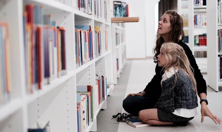 Läsambassadör Amanda Audas-Kass framför en bokhylla tillsammans med ett barn.